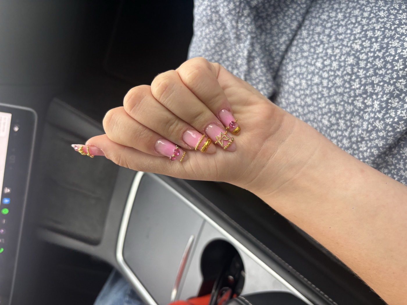 Square pink press-on nails with 3D gold charms, a bow, and pink gems